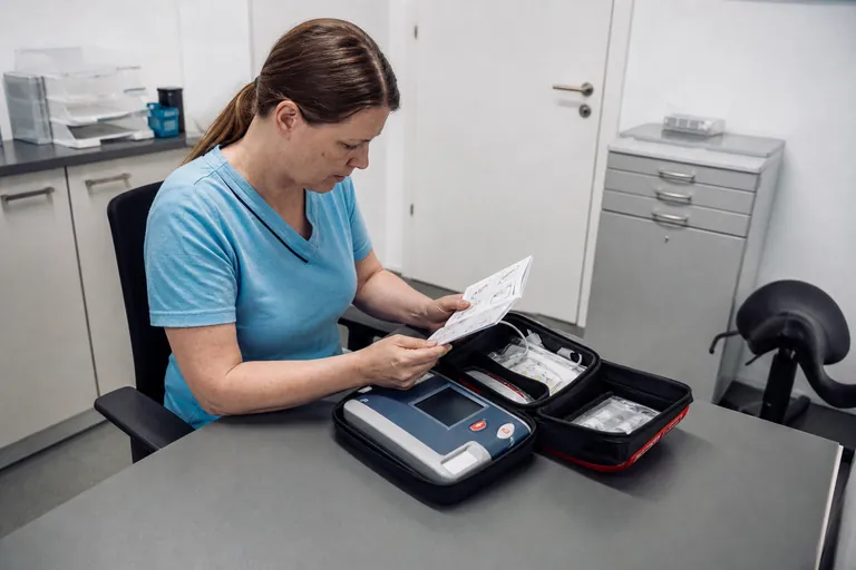 MFA gleicht Unterlagen mit einem Defibrillator in einem Praxisraum ab
